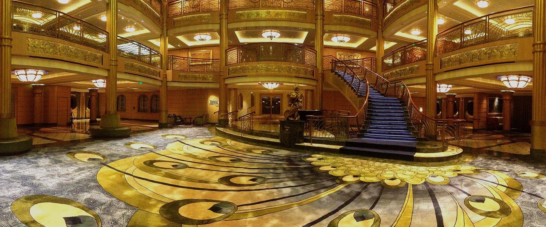 Three-deck Disney Fantasy atrium with sweeping staircase, bronze railings and peacock-pattern carpet